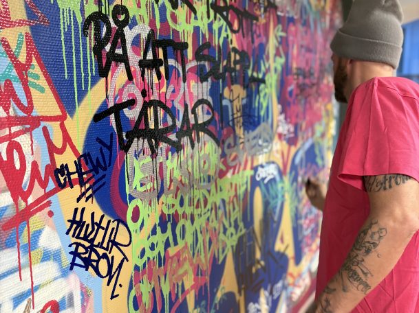 En graffare skriver på en vägg inomhus.